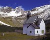 Kaple v horách se zasněženými vrcholky v pozadí.