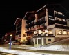 Hotel Monzoni v noci s vánoční dekorací a zasněženou krajinou.