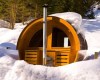 Dřevěná sudová sauna obklopená sněhem v lesním prostředí.