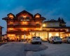 Večerní pohled na osvětlený hotel s parkovištěm a auty před ním.