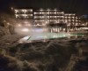 Osvětlený hotel s vyhřívaným bazénem a sněhem v popředí za tmavé noci.  