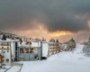 Zimní horská krajina s budovou hotelu pod zataženou oblohou při západu slunce.