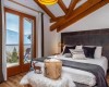 Ložnice s manželskou postelí, výhledem na hory, dřevěnými trámy a moderním dekorací.