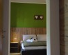 Pokoj s postelí, zelenou stěnou a dřevěným obložením, nad kterým visí dekorace se srdíčky.