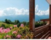 Dřevěný balkon s květinami a výhledem na hory s modrou oblohou a oblaky.