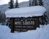 Dřevěná cedule hotelu S. Giusto pokrytá sněhem v zimní krajině.