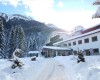 Zasněžený hotel obklopený zasněženými horami a stromy.