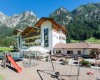 Moderní hotel s dětským hřištěm na pozadí hor.