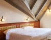 Pokoj pod šikmou střechou s manželskou postelí, dřevěným obložením a dvěma nástěnnými lampami.