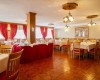 Restaurace s dřevěnými židlemi, bílými ubrusy a červenými závěsy.