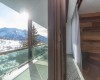 Výhled z okna na zasněžené hory a balkón s proskleným zábradlím.