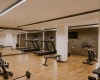 Fitness centrum s běžeckými pásy, činkami a stacionárním kolem na dřevěné podlaze.  