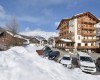 Dřevěný hotel ve zasněžené horské vesnici s řadou zaparkovaných aut.
