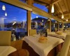 Interiér restaurace s prostřenými stoly a panoramatickými okny během soumraku.