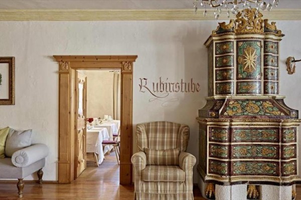 Historické kachlová kamna vedle proutěného křesla v rustikálním interiéru s nápisem 