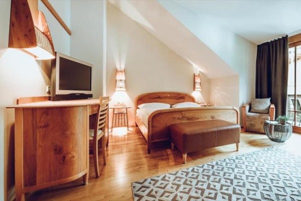 Moderní hotelový pokoj s dřevěným nábytkem, postelí, televizí a balkónovými dveřmi.