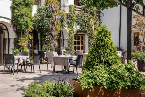 Venkovní terasa restaurace obklopená zelení s jídelními stoly.