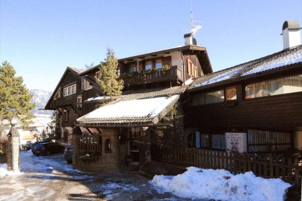 Dřevěný horský hotel s parkovacími místy, obklopený sněhem a stromy.