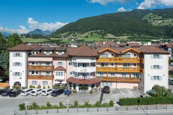Velký hotel s parkovištěm a horami v pozadí.