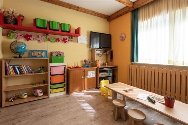 Dětský pokoj s nábytkem, hračkami a oknem s poloprůhlednými závěsy.