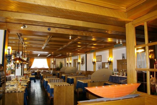 Interiér restaurace s dřevěnými stoly a stropem, modrými ubrusy a oranžovými závěsy.