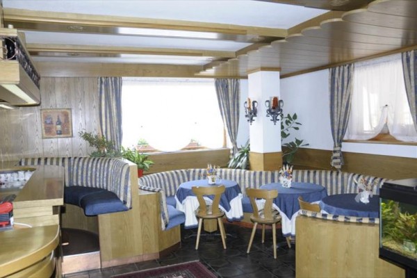 Restaurace s dřevěným interiérem, modrými pruhovanými sedačkami a kulatými stoly.