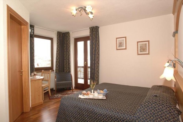 Hotelový pokoj s manželskou postelí, stolem a francouzskými dveřmi na balkon.