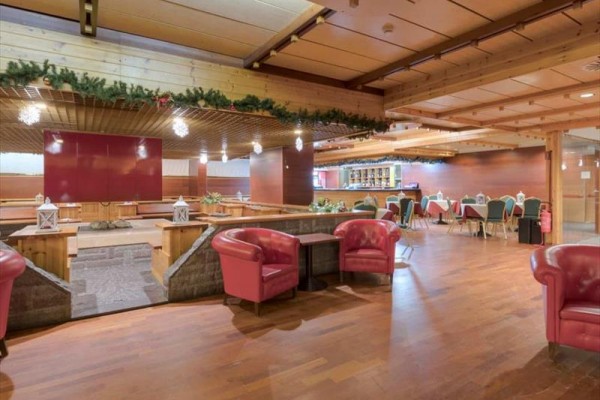 Hotelová restaurace s dřevěnými stropy a červenými křesly.