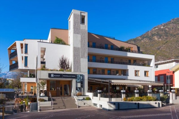 Moderní čtyřpatrový hotel na úpatí hory s terasou a venkovním posezením.  