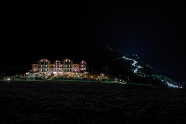 Noční osvětlený hotel u svahu s osvětlenou cestou.