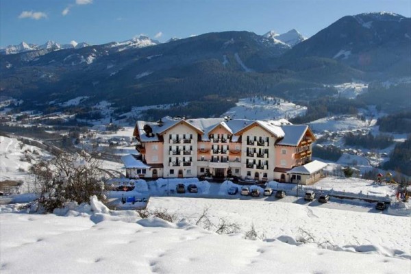 Hotel s bílou fasádou a balkony stojí na zasněženém svahu s horskou krajinou v pozadí.
