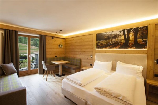 Moderní hotelový pokoj s dřevěným obložením, manželskou postelí a balkónem.