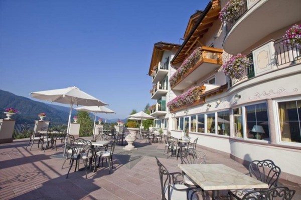 Venkovní terasa hotelu s kovovými stoly a židlemi, květinami a slunečníky.