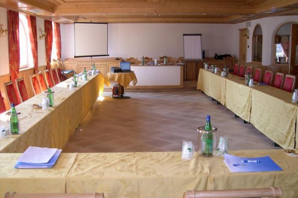 Konferenční místnost s uspořádáním do U, projekčním plátnem a notebookem na stole.