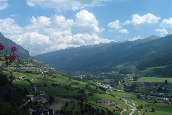 Horské panorama s údolím, vesnicemi a oblačnou oblohou.