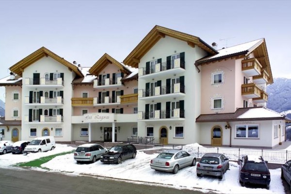 Budova hotelu se zasněženou střechou a několika auty zaparkovanými před ní.