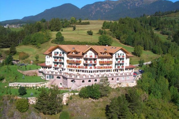 Hotel obklopený zelení a horami na pozadí.  