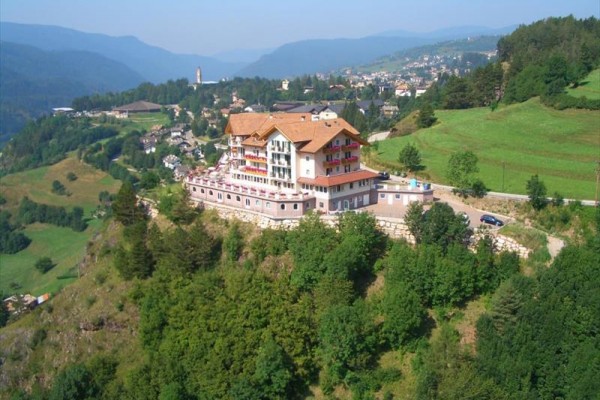 Hotel na vrcholu kopce obklopený zelenou krajinou a kopci v pozadí.