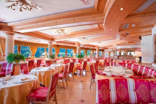 Elegantní restaurace s dřevěným stropem, červenými a zlatými prvky a kulatými stoly s ubrusy.