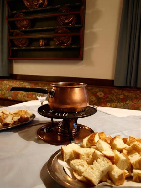 Měděný hrnec na fondue s talíři kostek chleba na stole.