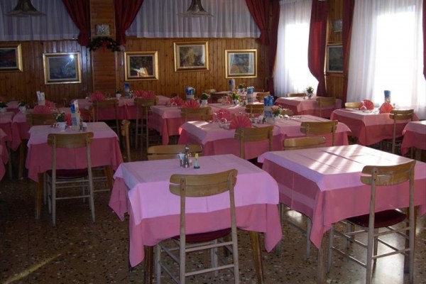 Restaurace s dřevěnými stoly pokrytými růžovými ubrusy a obrazy na stěnách.