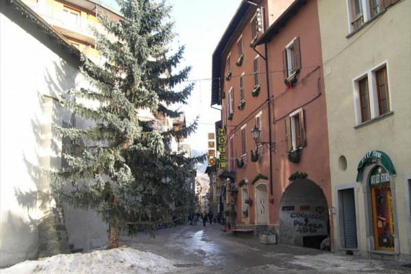 Úzká ulice s hotelem, stromečkem a sněhem na zemi.