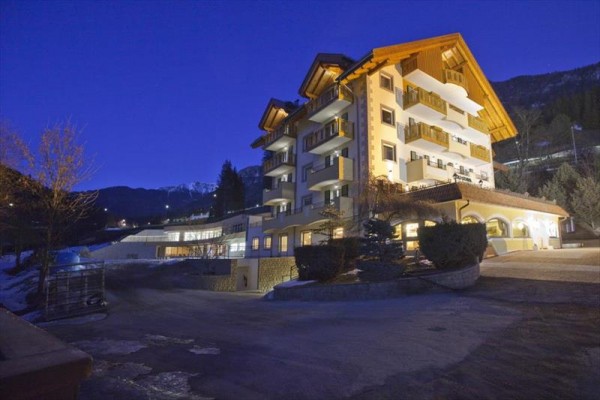 Velká budova hotelu v horské oblasti během soumraku, osvětlená umělými světly.