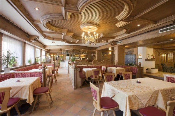 Stylová restaurace s dřevěným obložením a lustry, červené polstrované židle a ubrusy na stolech.