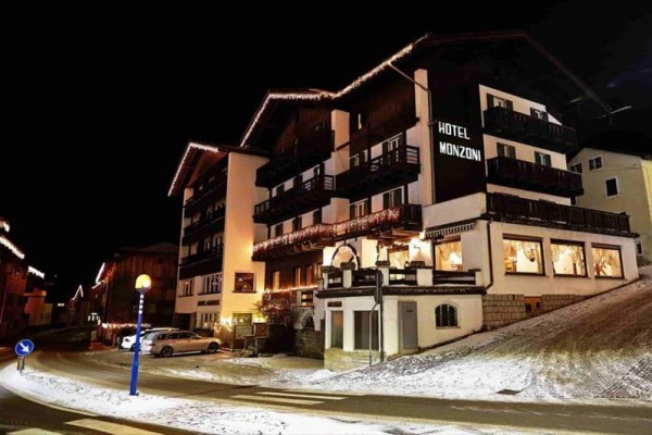 Hotel Monzoni v noci s vánoční dekorací a zasněženou krajinou.