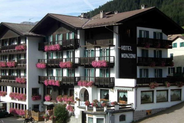 Hotel s dřevěnými balkóny zdobenými růžovými květinami.