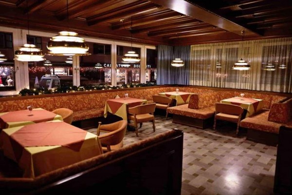 Restaurace s dřevěnými stropy, závěsy a prostřenými stoly s ubrusy.