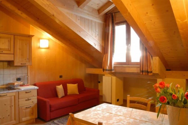 Podkrovní místnost s dřevěným obložením, červenou pohovkou a květinami na stole.