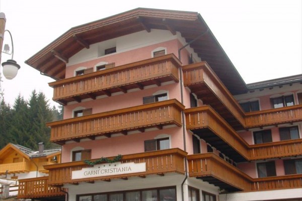 Čtyřpatrový horský hotel s dřevěnými balkony a růžovou fasádou.