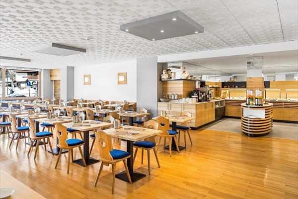 Moderní restaurace s dřevěnými stoly a židlemi s modrým čalouněním.